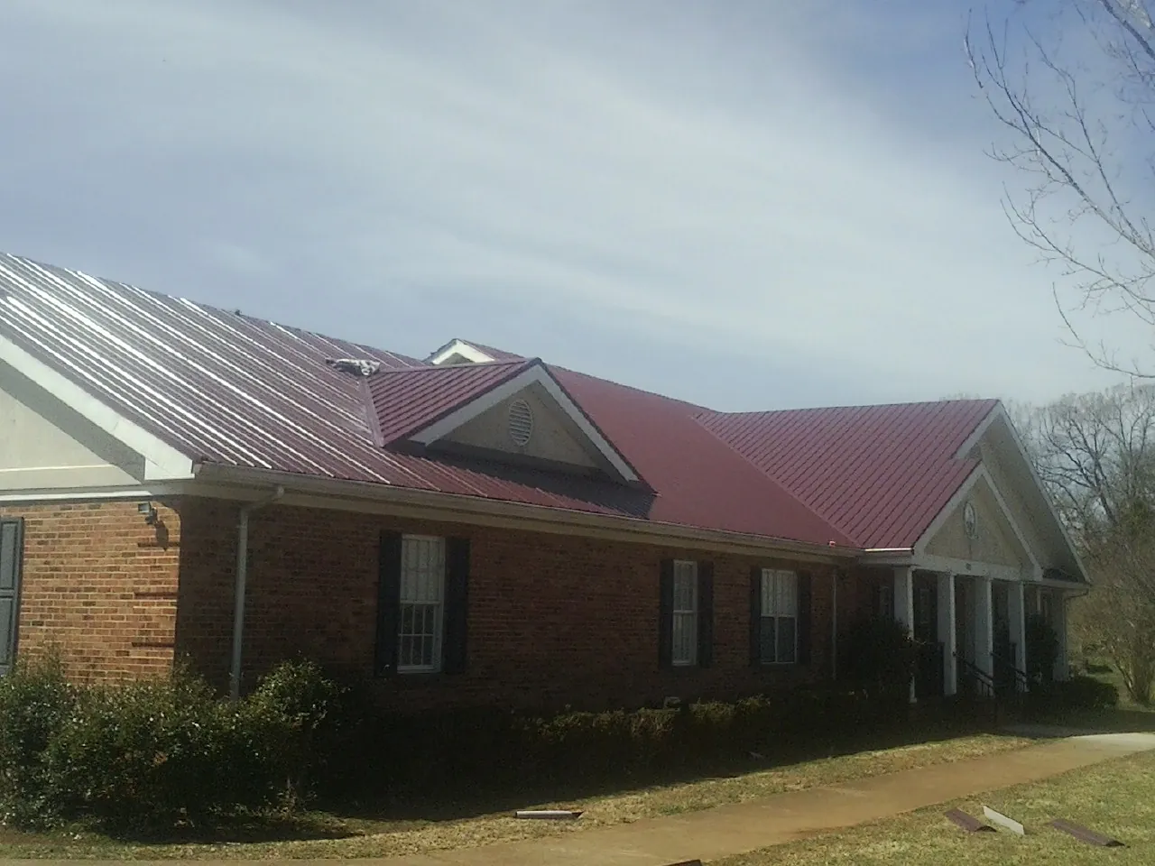 Red metal roof with gabled entries on a long brick building, from a Hail Damage Roof Repair job in Heber City
