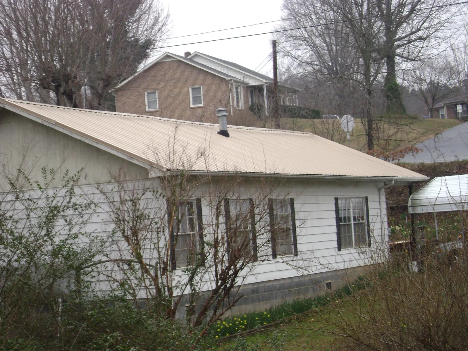 Tan metal roof on a white sided house set into a hillside — Commercial Roofing by Roofing Brothers in Heber City